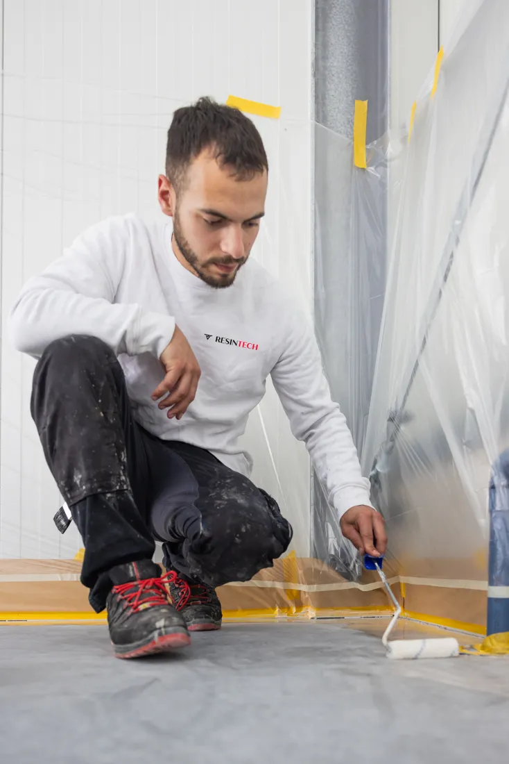 Ein Resintech-Mitarbeiter arbeitet mit einer Farbrolle und in der Hocke an der Beschichtung des Betonbodens im Lagerraum.